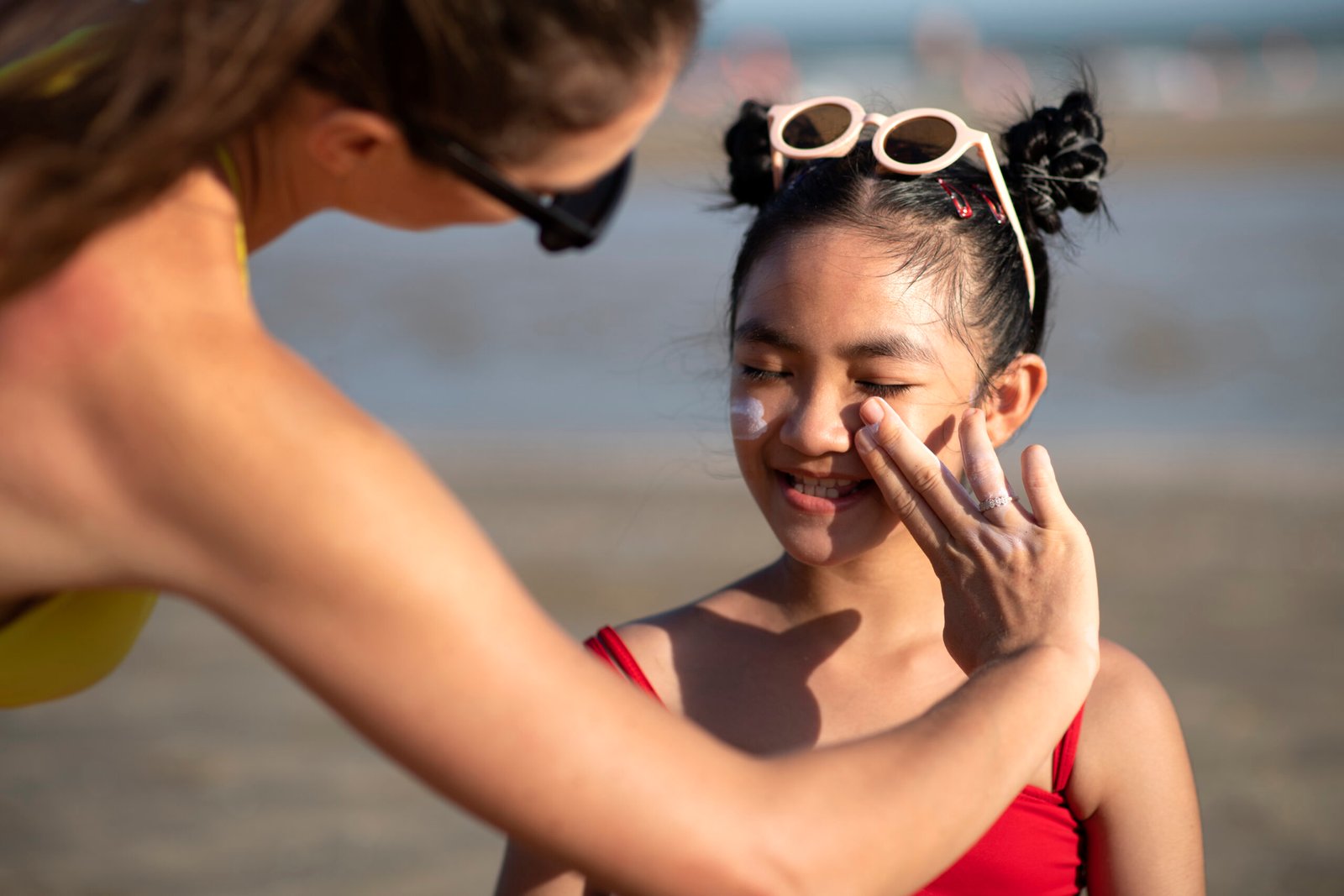 Mulher passando protetor solar no rosto de uma criança na praia